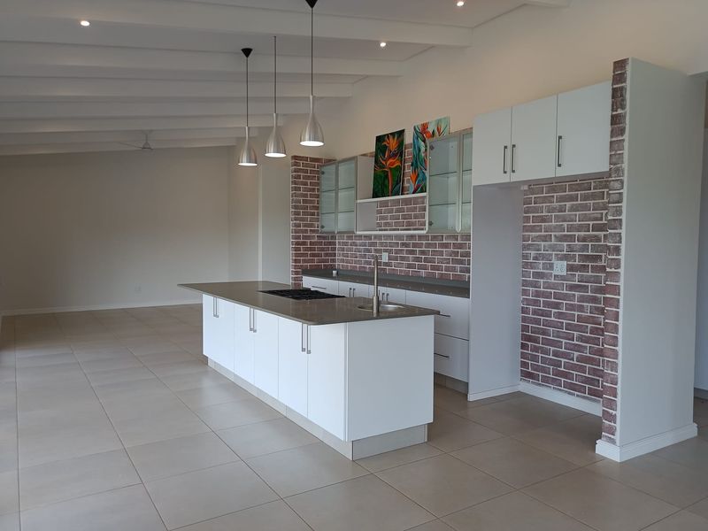 Modern open-plan kitchen featuring a central island, exposed brick accents, white cabinetry, and sleek tile flooring in a spacious, well-lit environment.