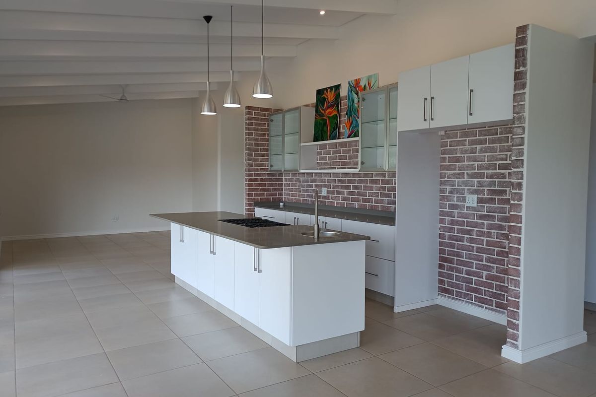 Modern open-plan kitchen featuring a central island, exposed brick accents, white cabinetry, and sleek tile flooring in a spacious, well-lit environment.