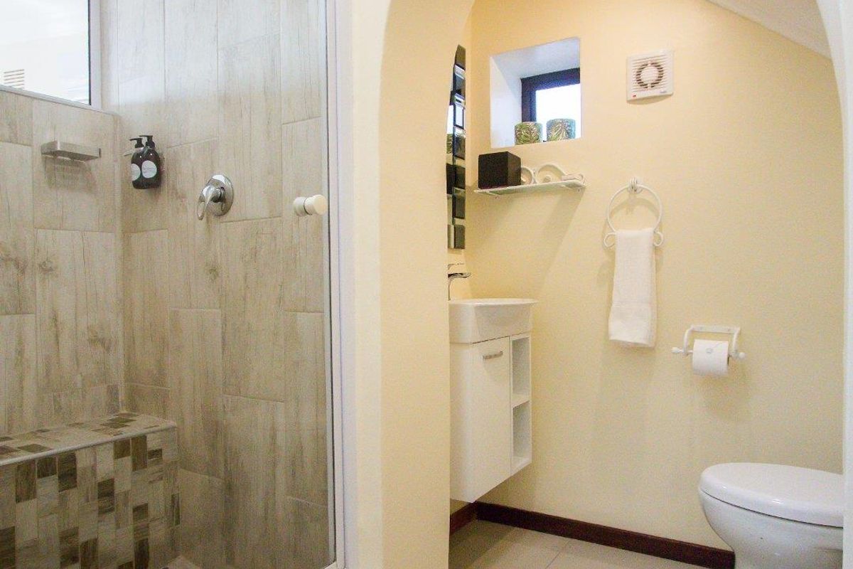A well-maintained bathroom featuring a glass-enclosed walk-in shower with a built-in tiled bench, a wall-mounted vanity, and a toilet set within an arched alcove.