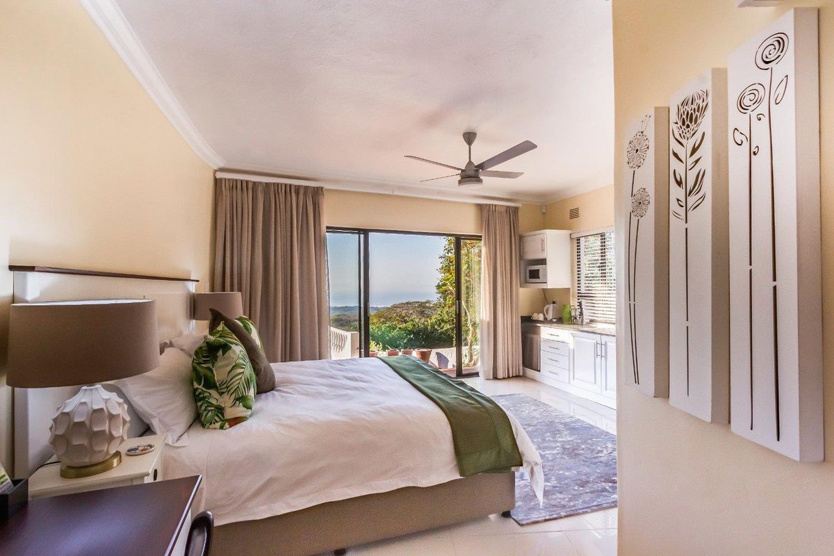 Spacious bedroom featuring a ceiling fan, integrated kitchenette area, and large sliding glass doors opening to a scenic outdoor view.