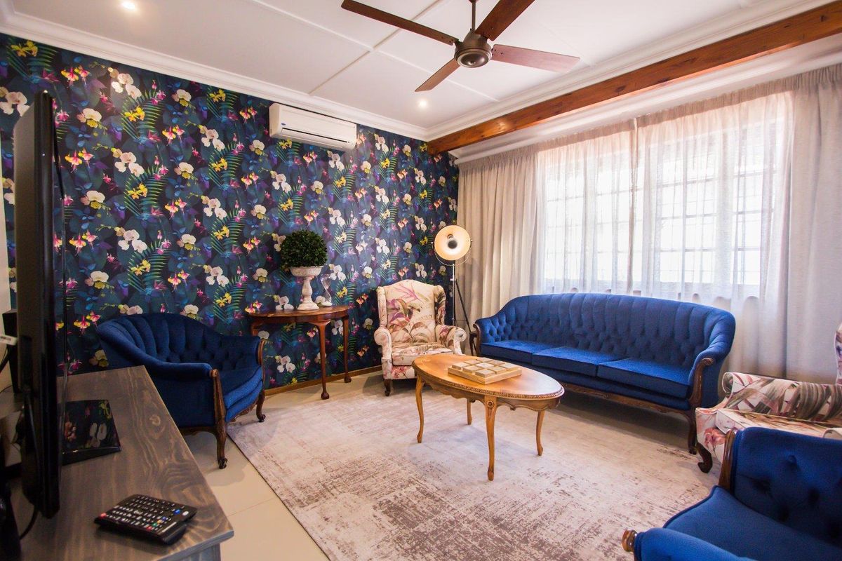 A cozy living room featuring a bold floral accent wall, a ceiling fan, and a wall-mounted air conditioning unit.