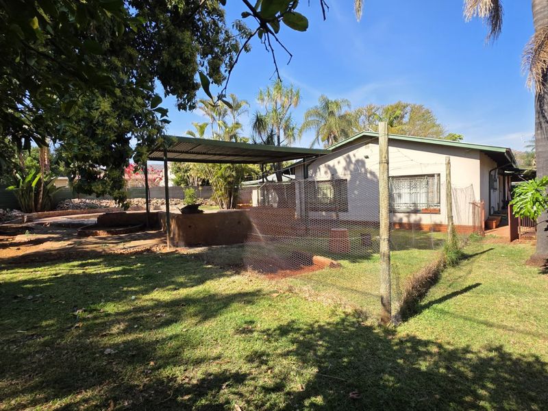 Rear view of the property featuring a covered patio area, established garden, and security features on the windows.