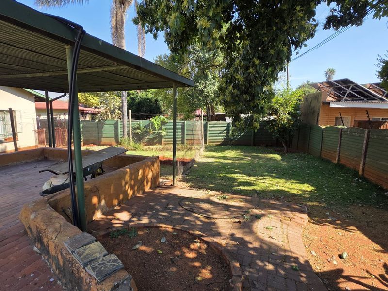Rear garden area featuring a covered patio with brick paving, a retaining wall, and perimeter precast concrete fencing.