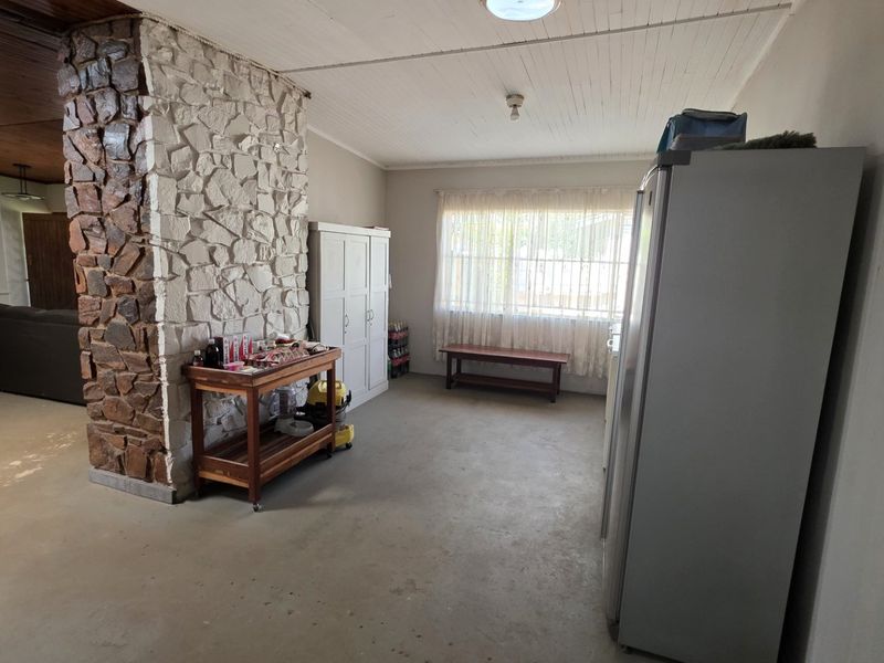 Open plan living area featuring a prominent stone fireplace wall, exposed timber ceiling, and concrete flooring, offering a rustic foundation for renovation.