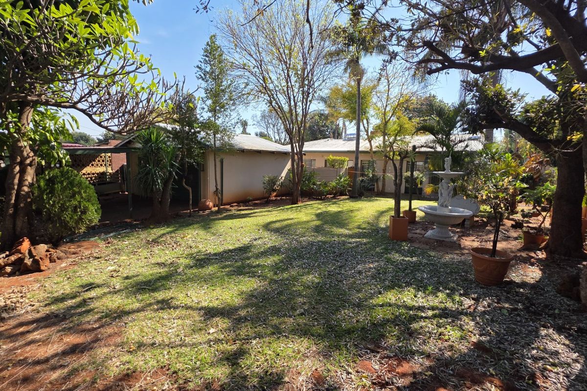 A spacious rear garden featuring mature trees, established landscaping, and a decorative stone fountain, providing a private outdoor setting.