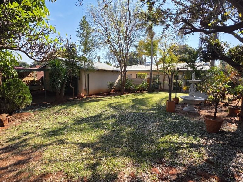 A spacious rear garden featuring mature trees, established landscaping, and a decorative stone fountain, providing a private outdoor setting.
