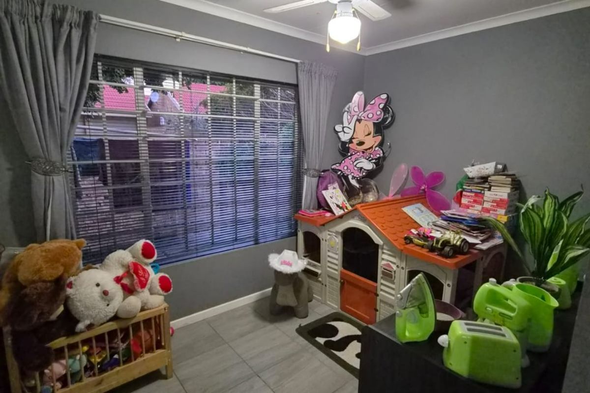 A bedroom featuring tiled flooring, a ceiling fan, and window blinds, currently utilized as a children's play area.