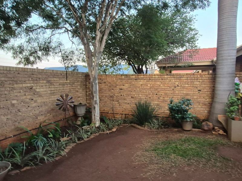 A private rear garden area featuring a brick boundary wall with electric fencing, mature trees, and a paved side walkway.