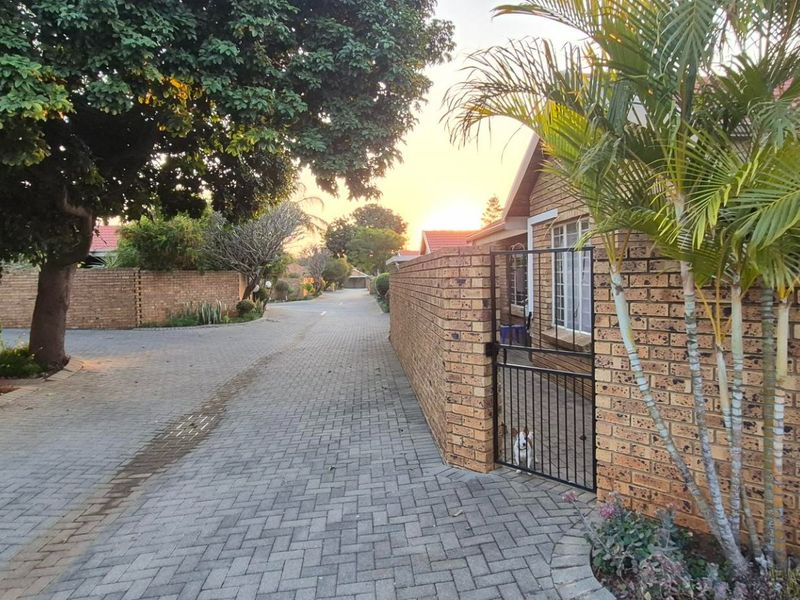 A view of the paved driveway and brick boundary walls leading towards the townhouse entrance at sunset.