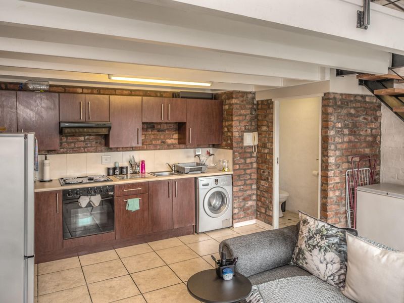 Open-plan kitchen featuring exposed brick walls, timber ceiling beams, and integrated appliances, seamlessly connected to the living area and staircase.