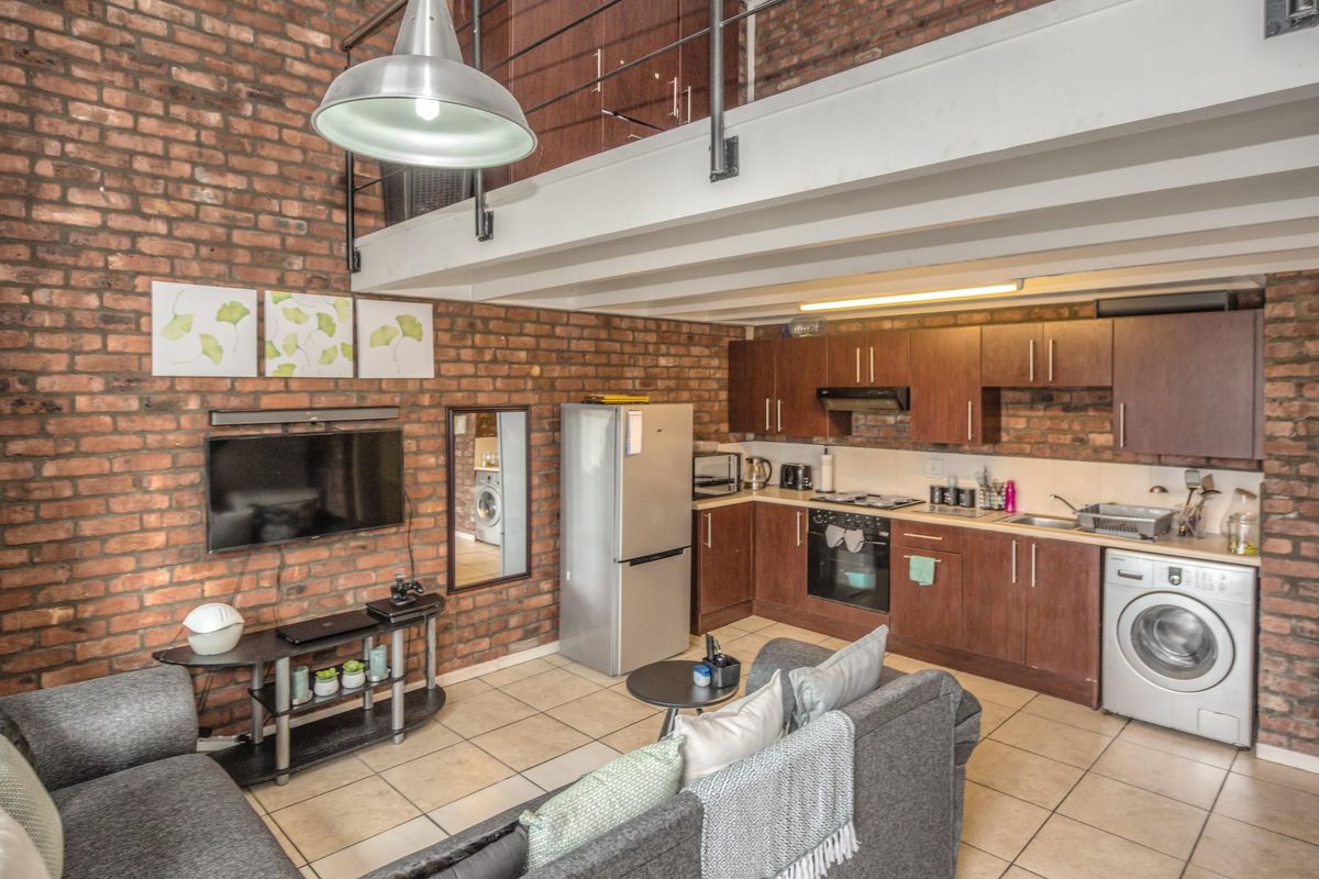 Open-plan living area featuring exposed brick walls, a mezzanine level, and a functional kitchen with built-in cabinetry and integrated appliances.