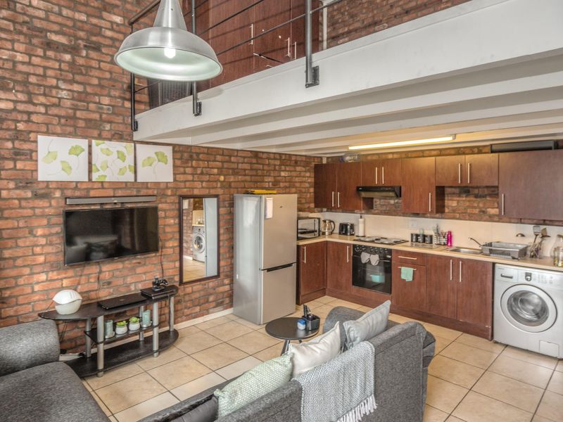 Open-plan living area featuring exposed brick walls, a mezzanine level, and a functional kitchen with built-in cabinetry and integrated appliances.
