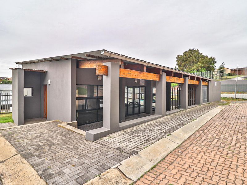 Exterior view of a communal clubhouse facility featuring exposed timber beam architecture, paved walkways, and secure aluminum-framed access points.