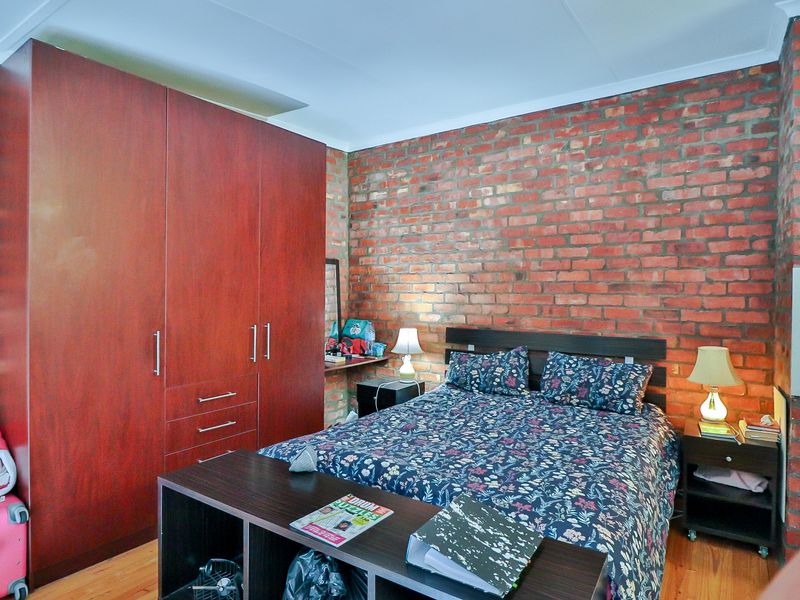 A bedroom featuring an exposed brick feature wall, laminate flooring, and a large built-in wardrobe providing ample storage space.