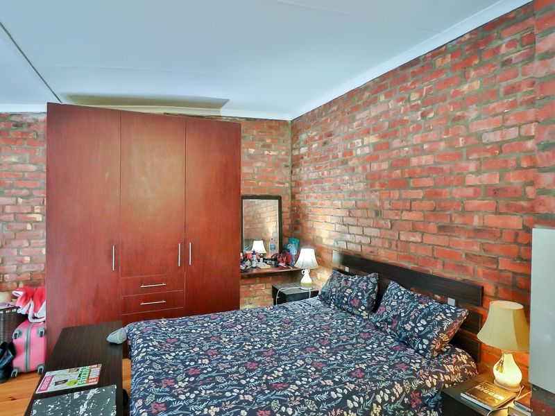 A bedroom featuring exposed brick walls and a large built-in wooden wardrobe, offering a rustic industrial aesthetic.