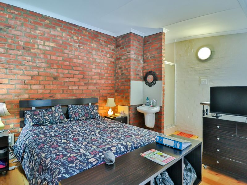 Bedroom featuring an exposed brick feature wall, integrated wall-mounted basin, and an adjoining shower enclosure with laminate flooring.
