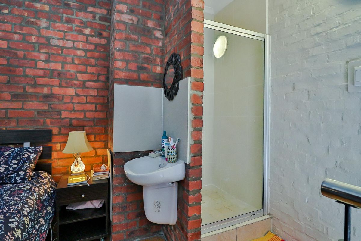 Bedroom featuring an exposed brick wall, integrated pedestal washbasin, and a compact shower enclosure with a glass door.
