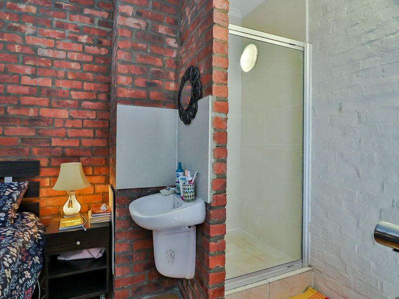 Bedroom featuring an exposed brick wall, integrated pedestal washbasin, and a compact shower enclosure with a glass door.