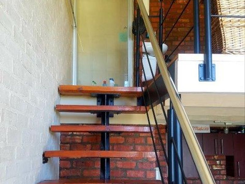 Industrial-style apartment interior featuring an exposed brick wall, timber staircase with metal railing, and a view toward a shower enclosure.