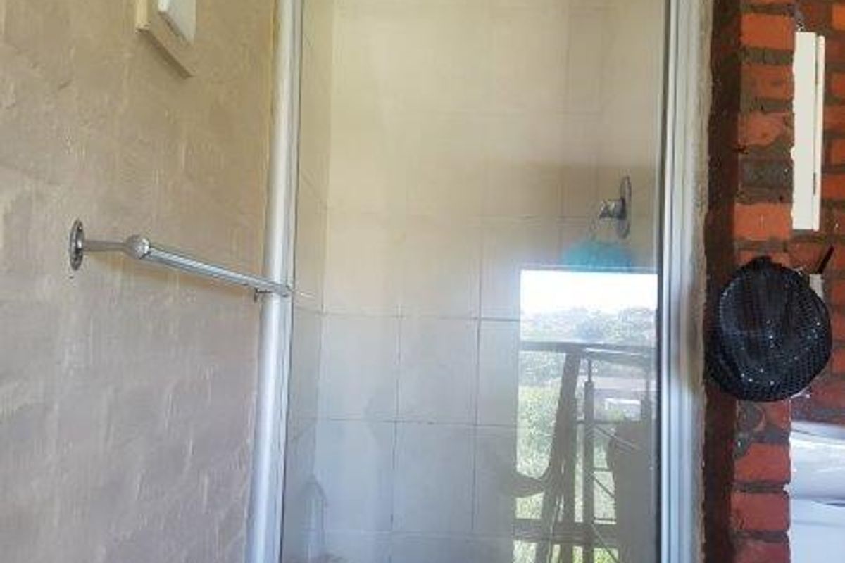 A bathroom shower enclosure featuring tiled walls, a glass door, and exposed brickwork detailing.
