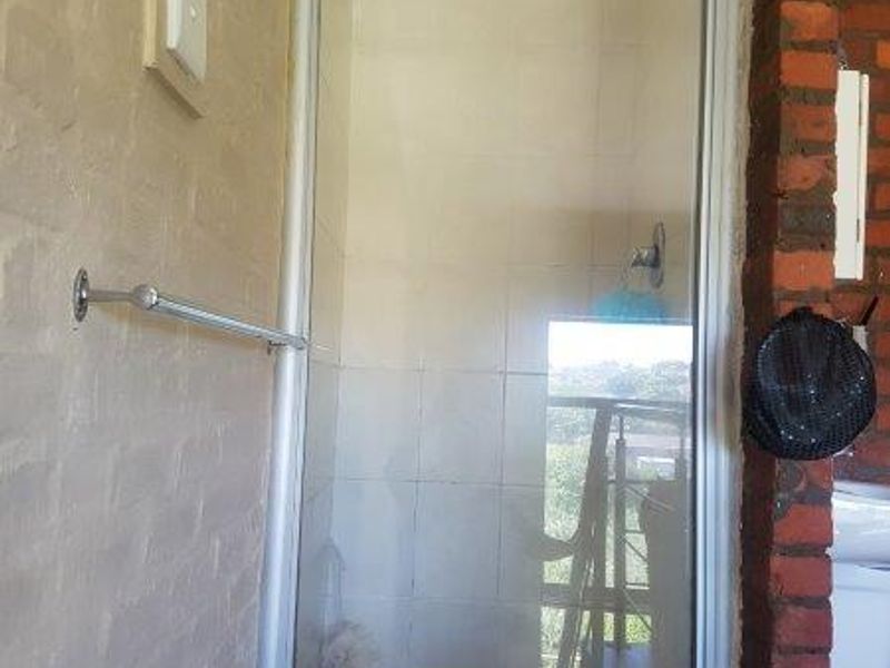 A bathroom shower enclosure featuring tiled walls, a glass door, and exposed brickwork detailing.