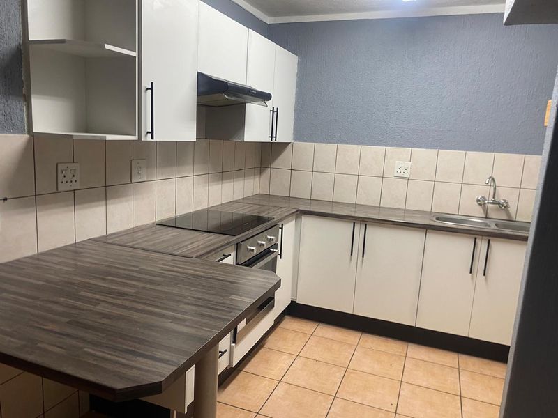 A clean, functional kitchen featuring white cabinetry, dark laminate countertops, an integrated electric hob, oven, and a tiled backsplash.