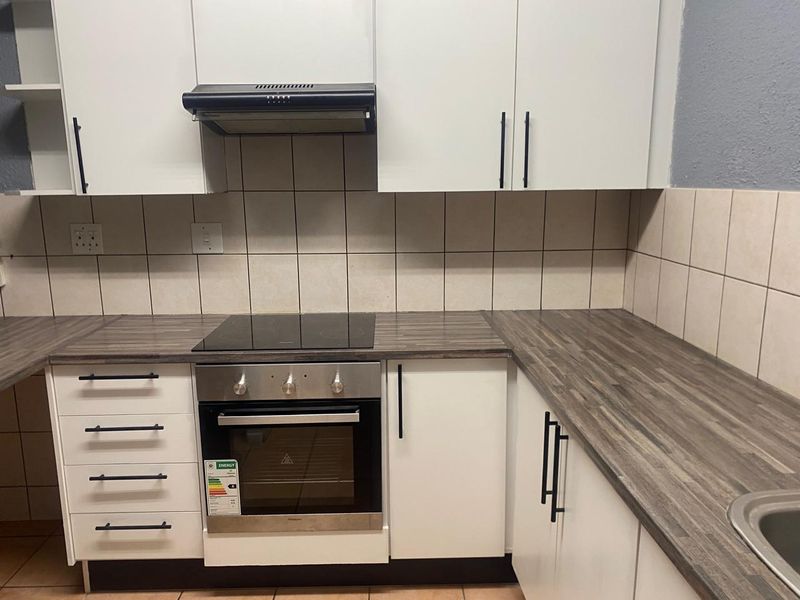 A clean and functional kitchen featuring white cabinetry, wood-look laminate countertops, a built-in oven, electric hob, and a tiled backsplash.