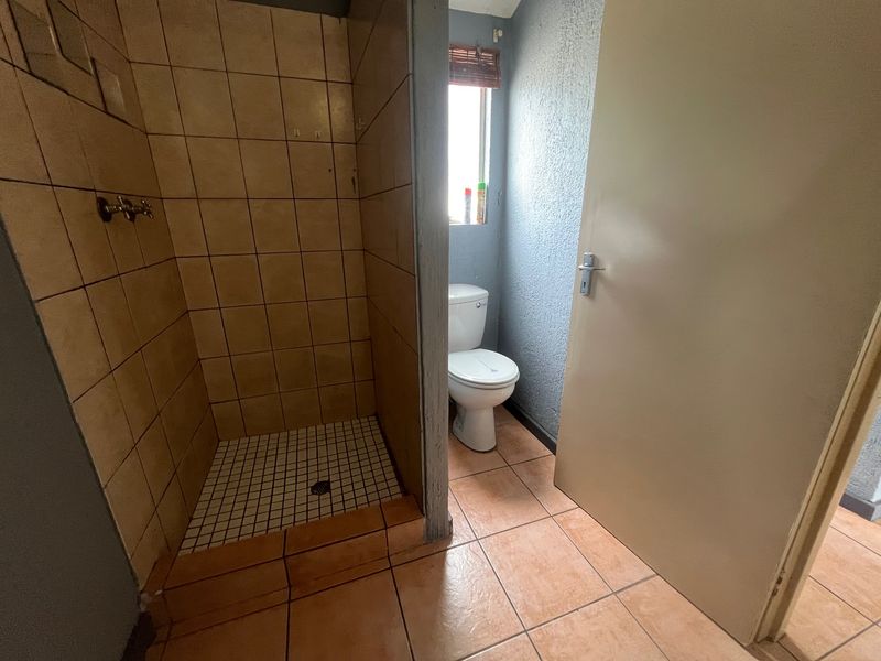 A functional bathroom featuring a tiled shower enclosure and a standard toilet, finished with ceramic floor tiles and textured wall surfaces.