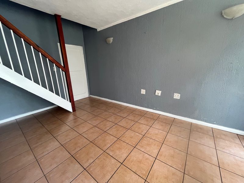 An empty living area featuring tiled flooring, a staircase with a wooden handrail, and grey textured walls with integrated lighting.