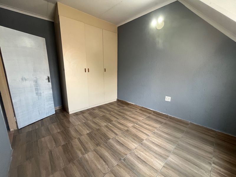 An empty bedroom featuring wood-look tiled flooring, a built-in wardrobe, and grey painted walls with a sloped ceiling detail.