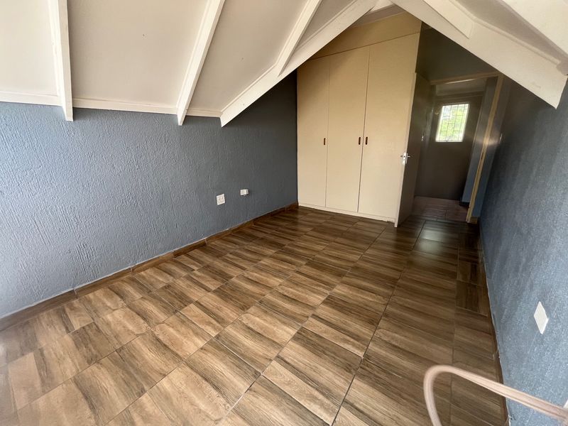 An empty bedroom featuring wood-look tiled flooring, built-in cupboards, and a sloped ceiling with exposed rafters.