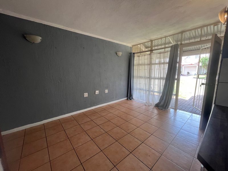 An empty living room featuring ceramic floor tiles, wall-mounted lighting, and direct access to the exterior through a security gate and glass sliding door.