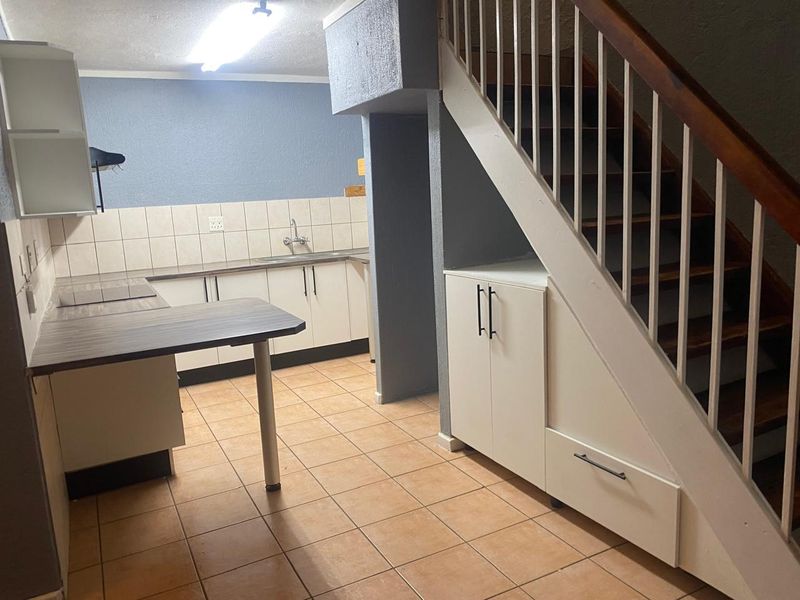 Functional kitchen area featuring built-in cabinetry, tiled backsplash, and convenient under-stair storage, situated adjacent to the staircase.