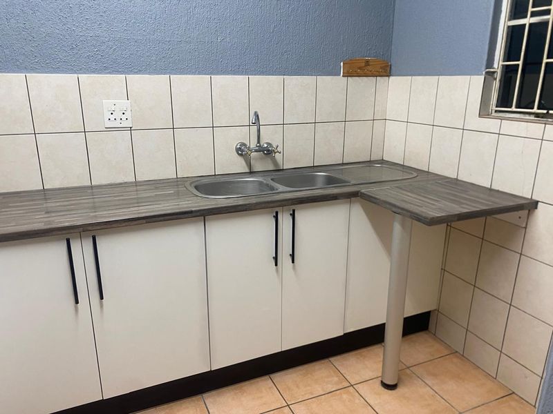A clean and functional scullery area featuring built-in base cabinetry, a double bowl stainless steel sink, and neutral ceramic wall and floor tiling.