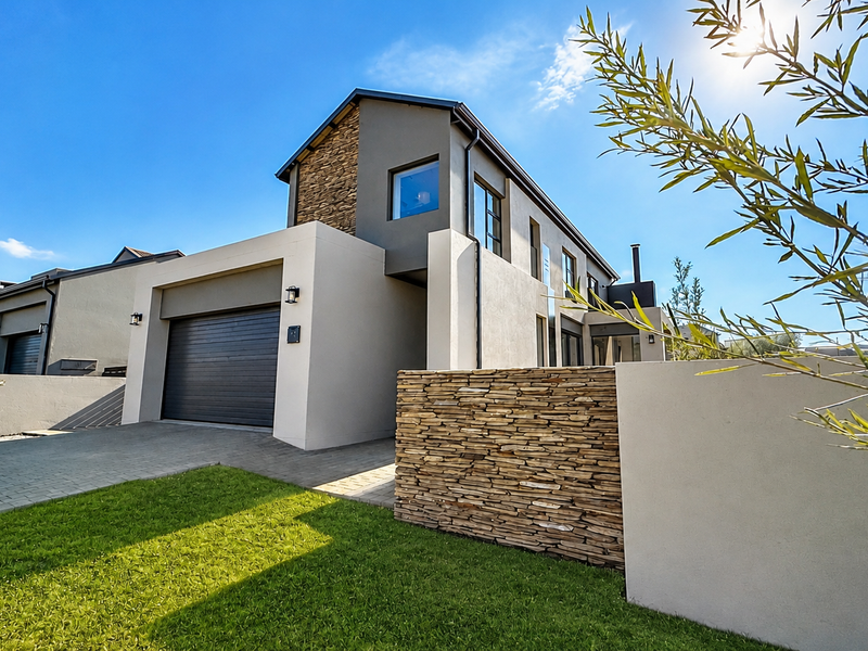 Modern double-story residential facade featuring stone cladding accents, a paved driveway, and a secure sectional garage door.