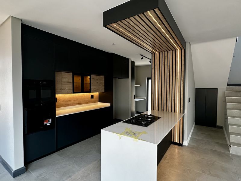 Modern kitchen featuring matte black cabinetry, stone countertops, a gas hob, and a striking timber slat feature wall with integrated lighting.