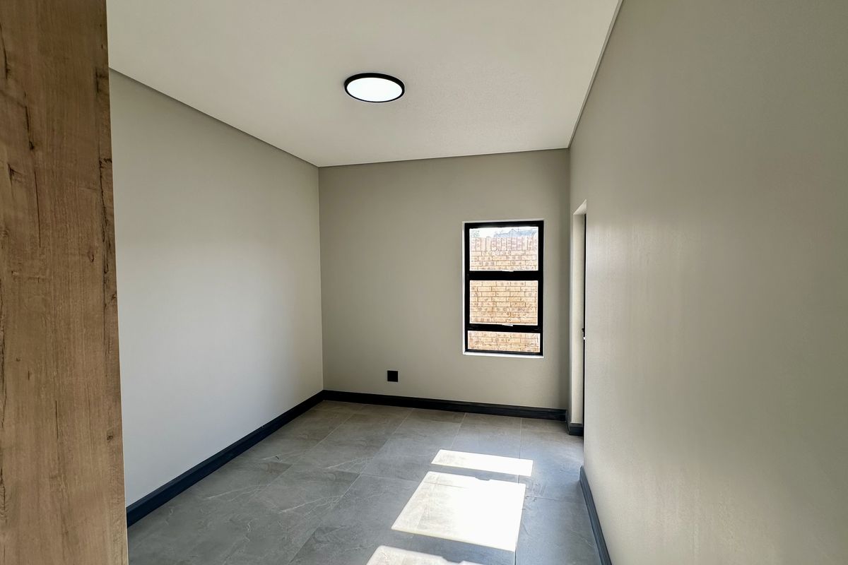 A clean, modern, and empty bedroom featuring neutral walls, large format floor tiles, and a contemporary flush mount ceiling light.