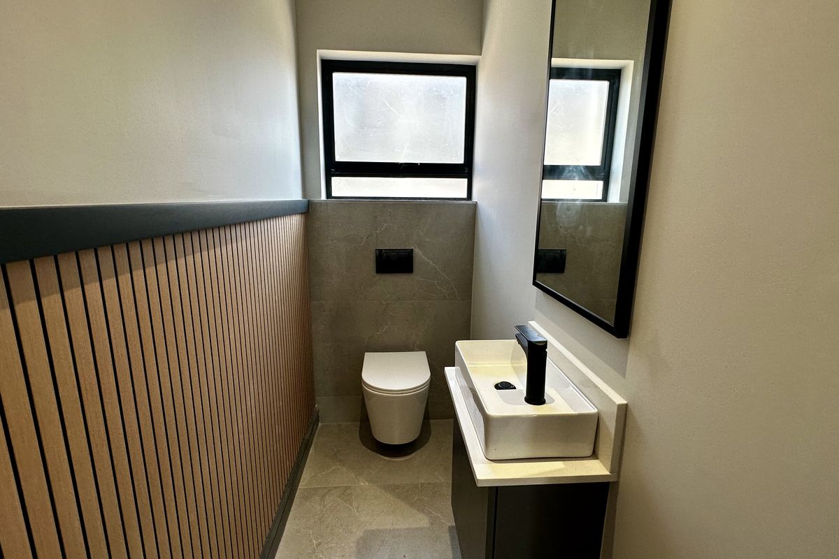 Modern guest bathroom featuring a wall-mounted toilet, vessel sink with black fixtures, and stylish slatted wood wall paneling.