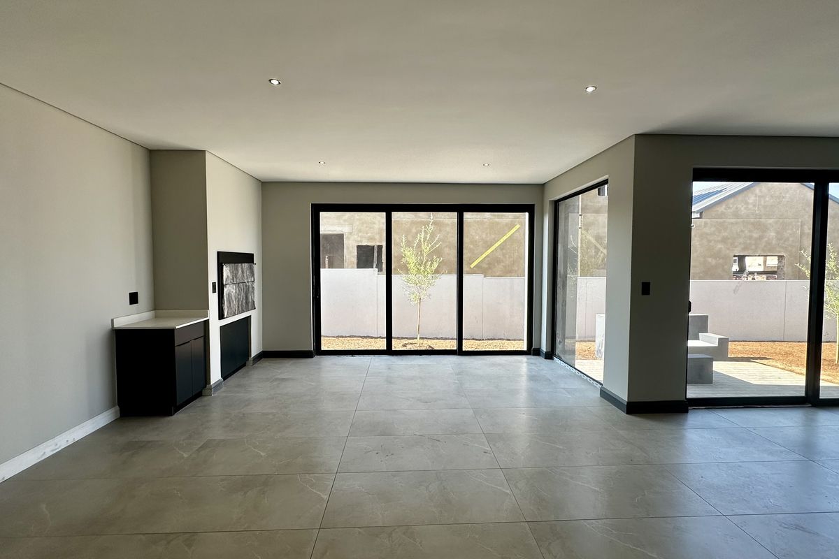 Spacious, modern open-plan living area featuring large format floor tiles, recessed lighting, built-in cabinetry, and expansive sliding glass doors leading to the garden.