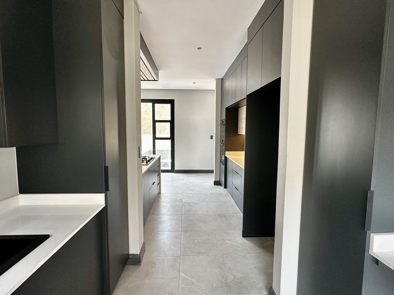 Modern, minimalist kitchen featuring sleek dark cabinetry, stone countertops, integrated appliances, and large-format porcelain floor tiles in a clean, open-plan layout.