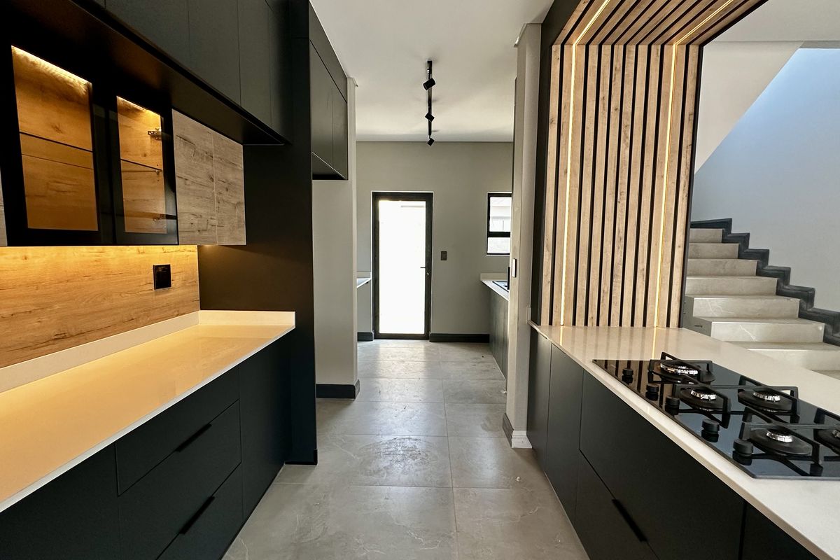 Modern kitchen featuring sleek matte black cabinetry, stone countertops, integrated gas hob, and a stylish timber slat feature wall with ambient lighting.
