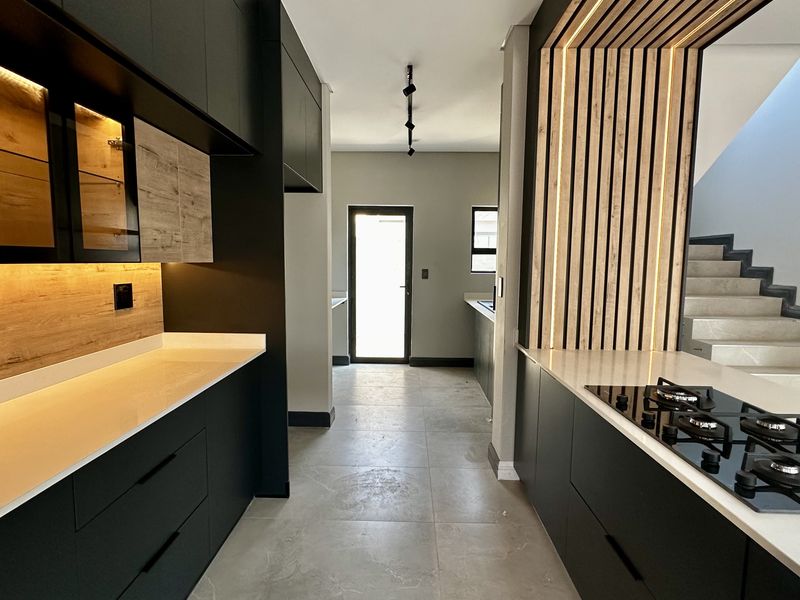 Modern kitchen featuring sleek matte black cabinetry, stone countertops, integrated gas hob, and a stylish timber slat feature wall with ambient lighting.