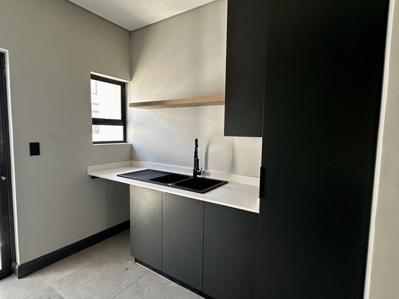 Modern scullery featuring sleek dark cabinetry, white stone countertops, a double sink with a black mixer tap, and a floating timber shelf.