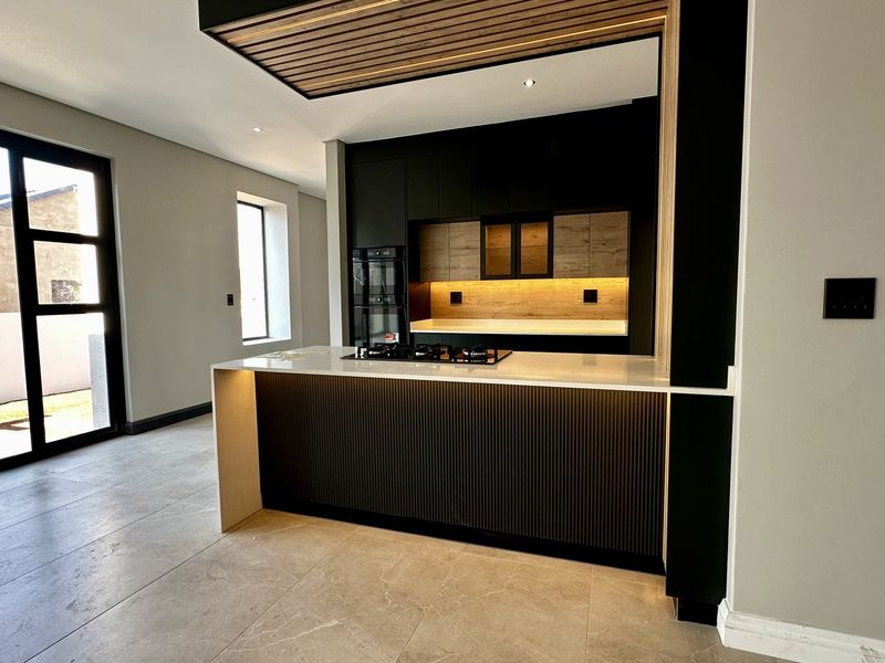 Modern open-plan kitchen featuring a central island with gas hob, stone countertops, integrated oven, and stylish slatted timber ceiling detail.