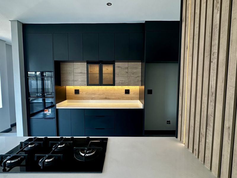 Modern kitchen featuring dark cabinetry, stone countertops, built-in oven, gas hob, and a stylish slatted wood feature wall with integrated lighting.