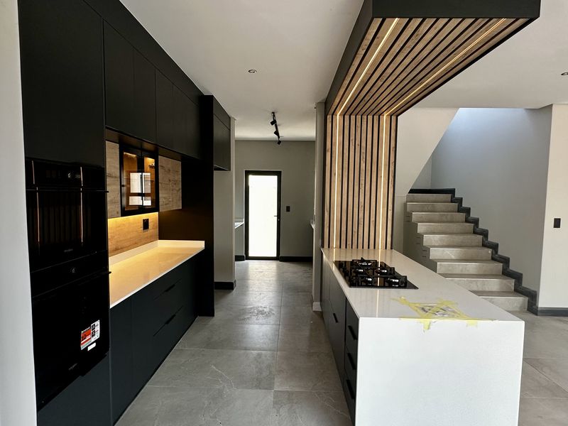 Modern kitchen featuring matte black cabinetry, stone countertops, a gas hob, and a striking timber slat feature wall with integrated lighting.