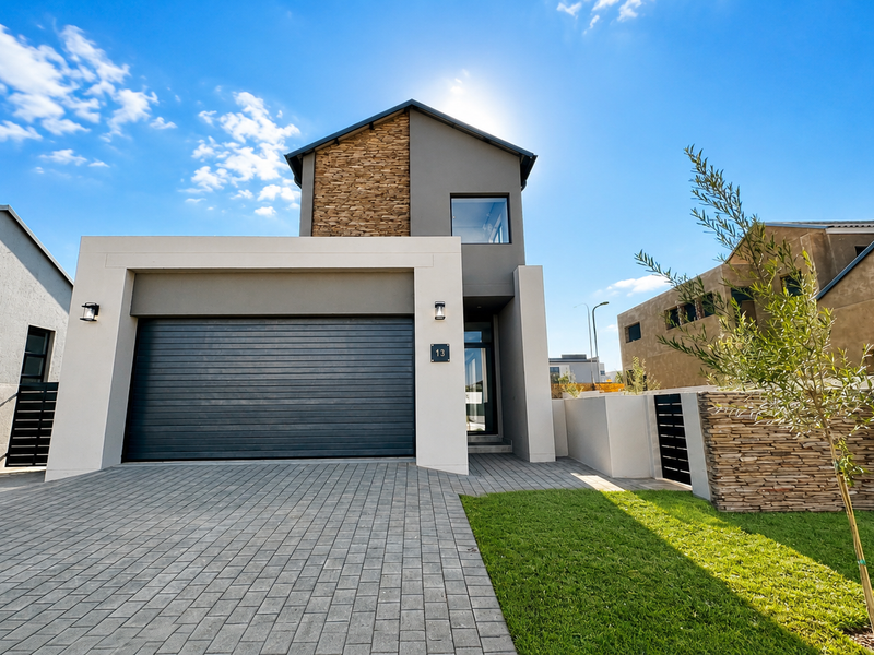 Modern double-storey residential facade featuring a paved driveway, integrated garage, and contemporary stone cladding accents.