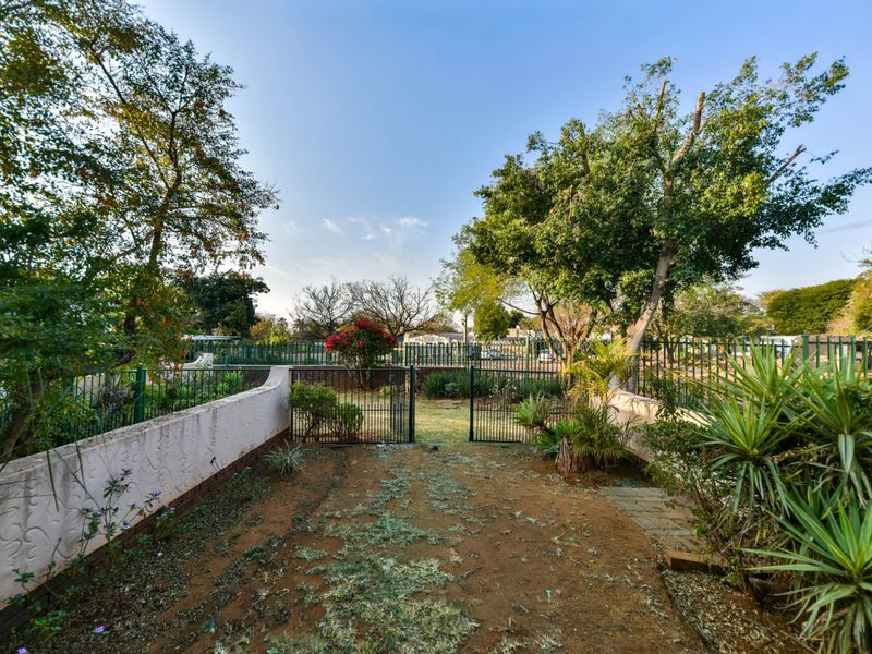A rear garden area featuring a metal gate, perimeter fencing, and a masonry boundary wall with mature trees and established landscaping.