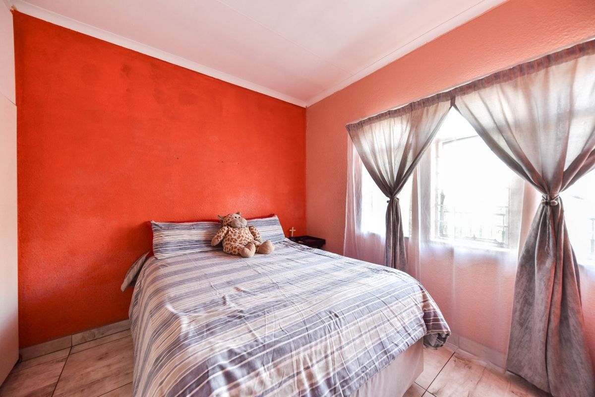 A bedroom featuring tiled flooring, a window with security bars, and a bold accent wall, offering a functional space ready for cosmetic updates.