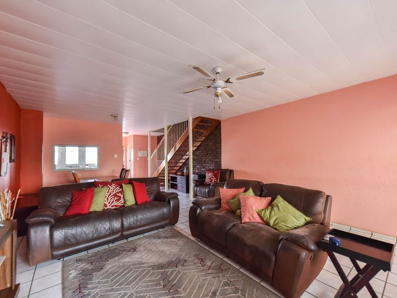 Spacious living area featuring tiled floors, a central ceiling fan, and an exposed brick staircase feature wall, offering a functional open-plan layout.